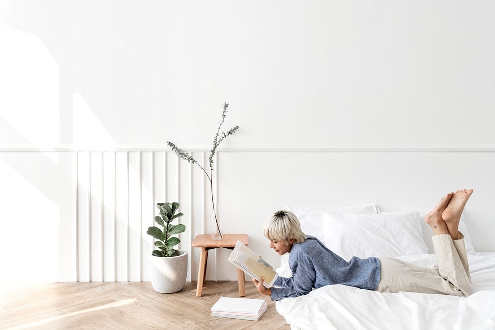 Blond haired Asian woman reading a book on a mattress on the floor