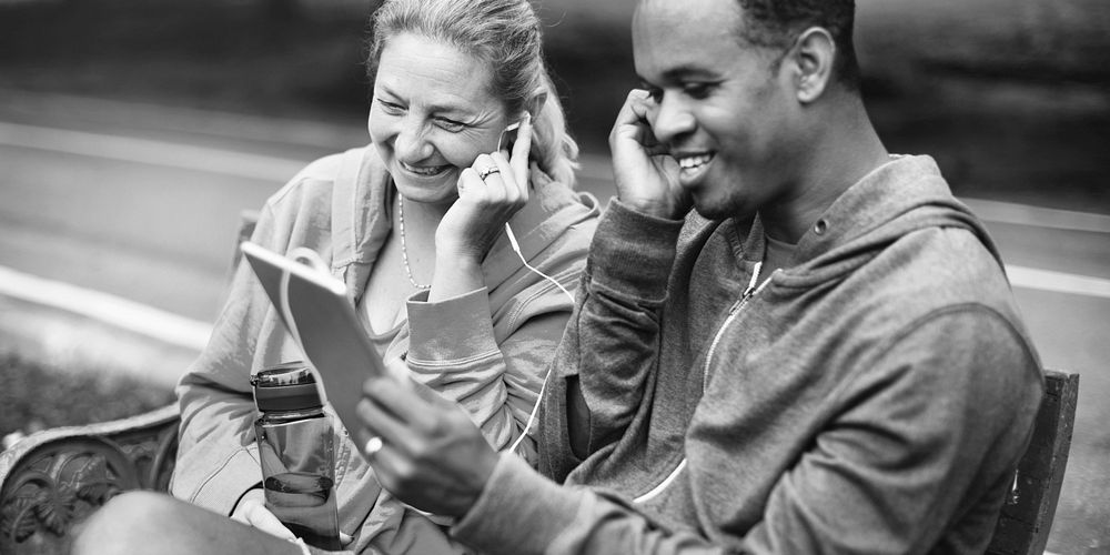 Couple cheerfully listening to music sitting on a park bench