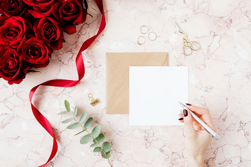 Woman writing on a card mockup by a bouquet of red roses 
