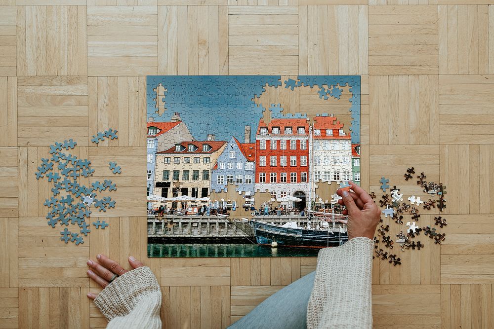 Woman assembling a jigsaw puzzle of Nyhavn, Copenhagen during coronavirus quarantine.