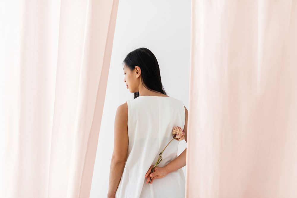 Asian woman with a dry pink peony flower in a hand among the pink curtain