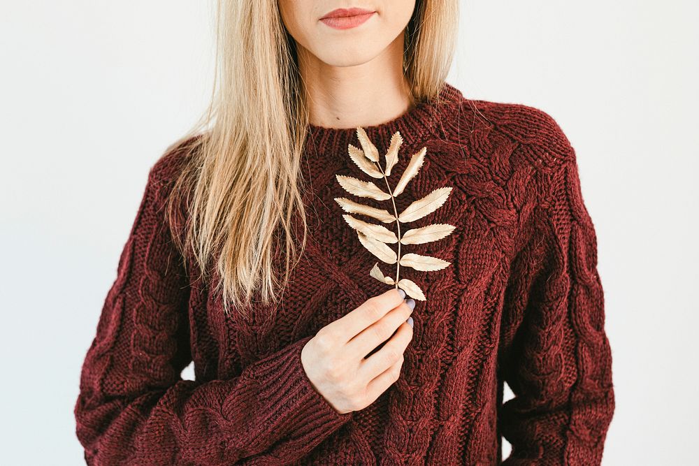Blonde woman wearing a cozy sweater holding golden crisp leaves 