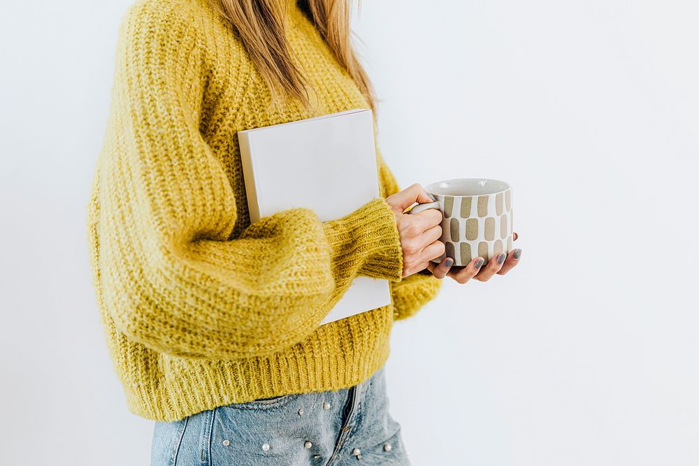 Woman wearing a cozy yellow sweater with a notebook and a cup of warm tea 