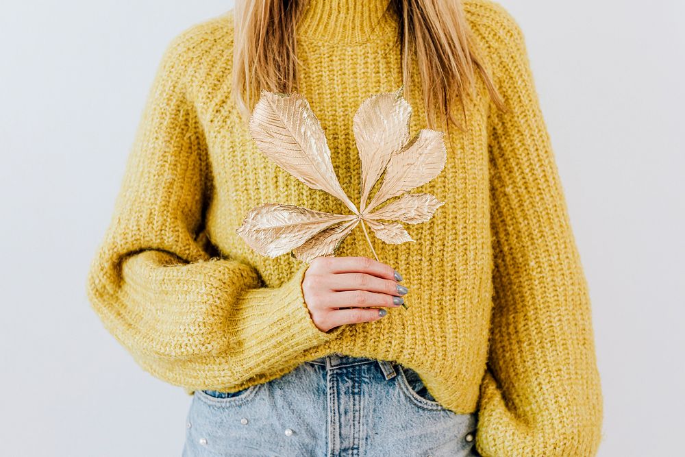 Woman in a yellow knitted sweater holding a golden crisp leaf 