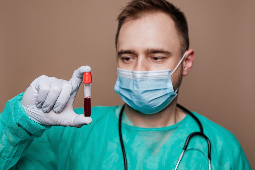 Surgeon wearing a mask holding a blood test tube 