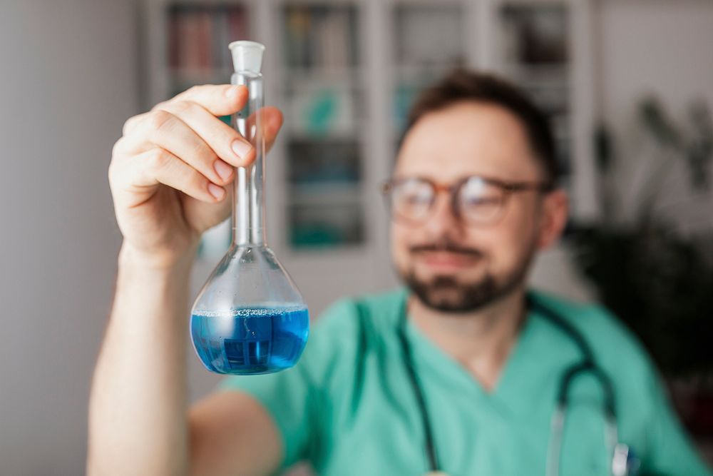 Microbiologist in a green gown holding a volumetric flask
