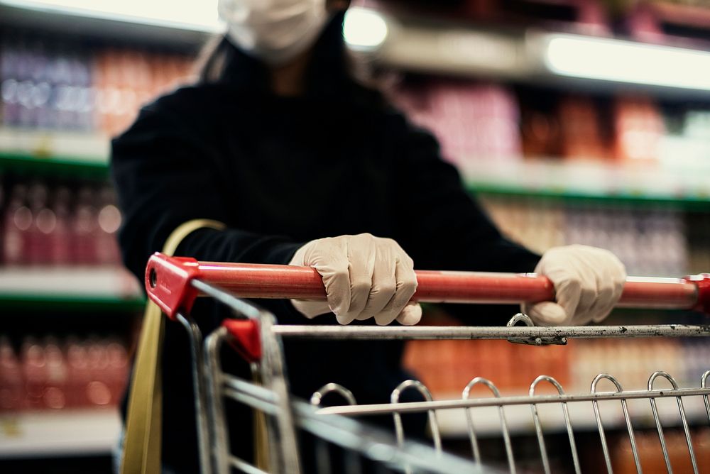 Hand wearing a latex glove while pushing a shopping cart to prevent coronavirus contamination