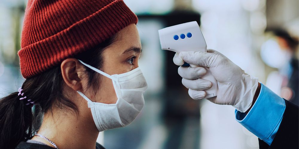 Woman in a medical mask getting her temperature measured by an electronic thermometer coronavirus banner 