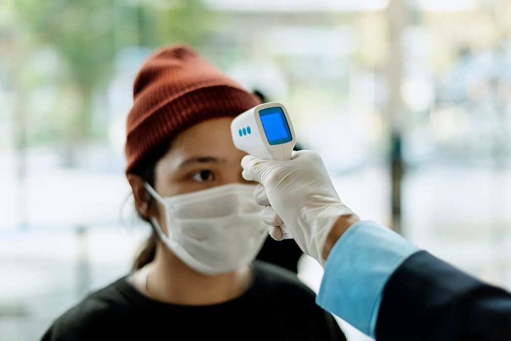 Woman in a medical mask getting her temperature measured by an electronic thermometer 