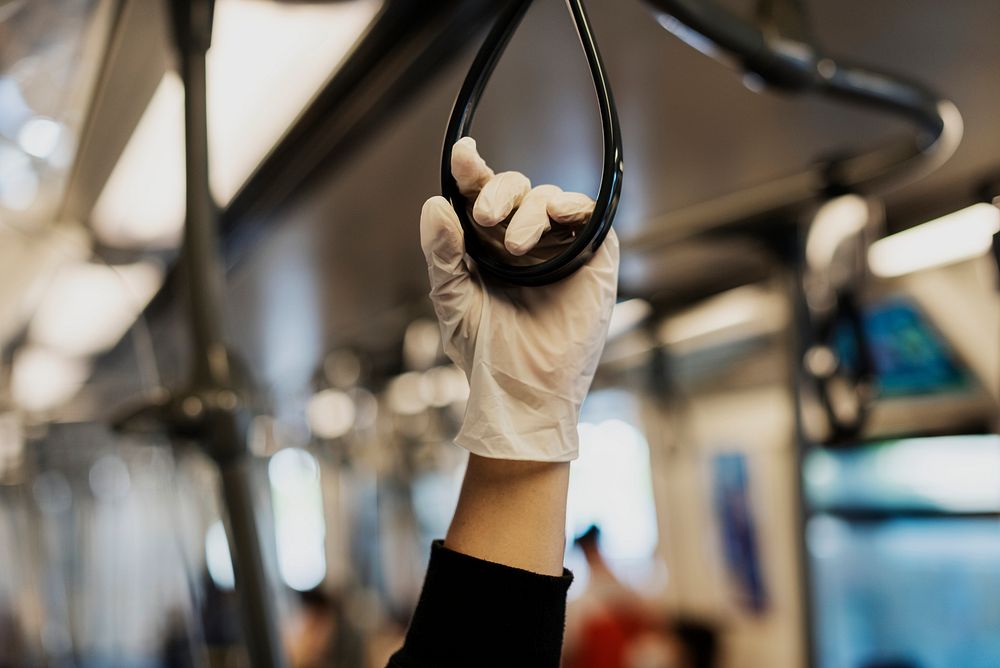 Hand wearing a latex glove while holding a train handrail  to prevent coronavirus contamination