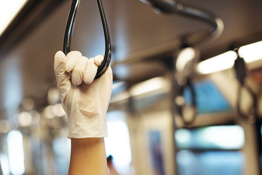 Hand wearing a latex glove while holding a train handrail  to prevent coronavirus contamination