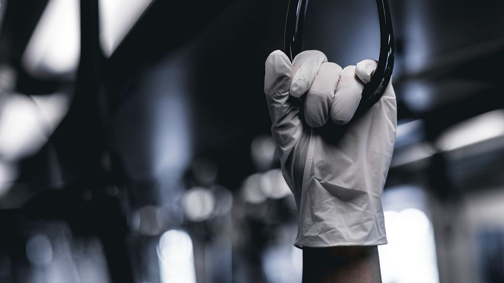 Hand wearing a latex glove while holding a train handrail  to prevent coronavirus contamination