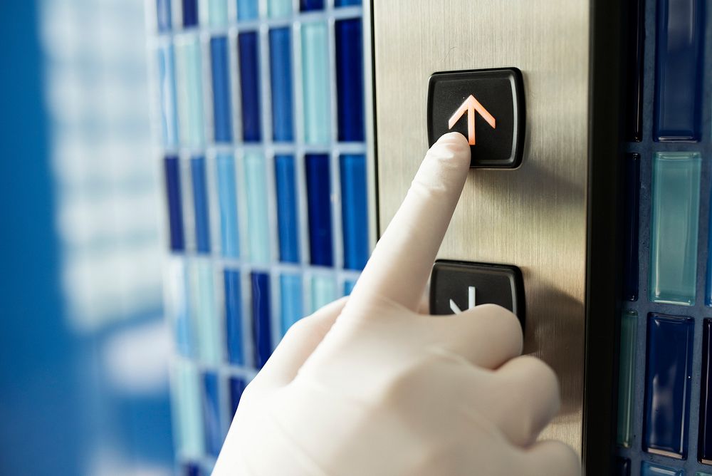 Gloved hand pressing an elevator button to prevent coronavirus contamination