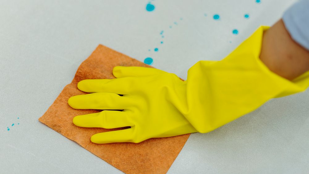 Woman wearing yellow rubber gloves and cleaning the surface