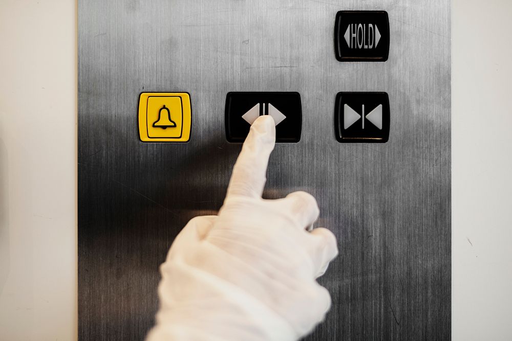 Gloved hand pressing an elevator button to prevent coronavirus contamination