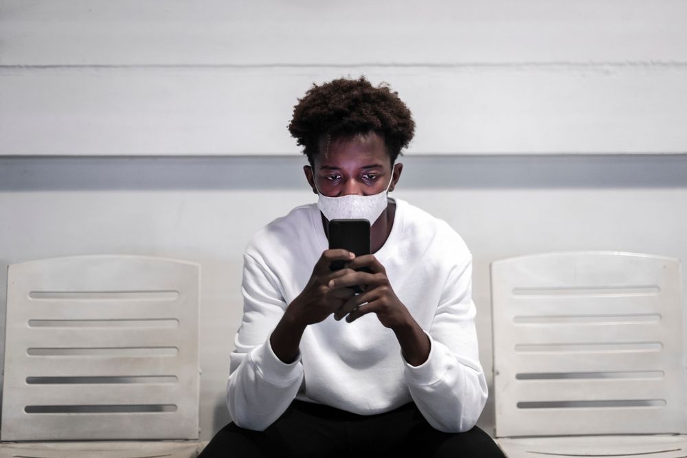 Young African American man sitting alone and texting on his smartphone