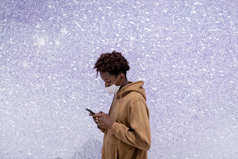 Young man using his phone by a purple glitter wall