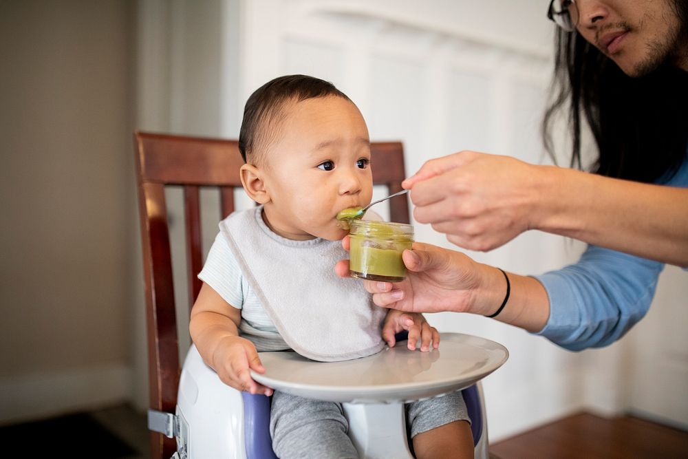 Dad feeding his son with baby puree on a highchair
