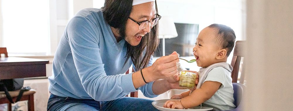 Asian father feeding his son with baby puree social banner