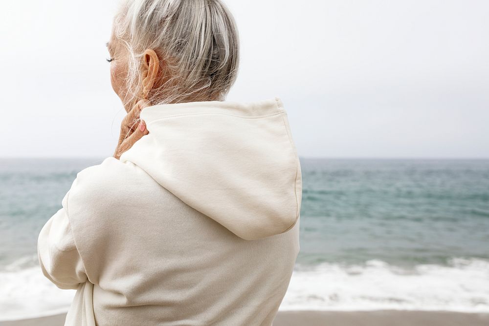 Senior woman in hoodie relaxing at the beach