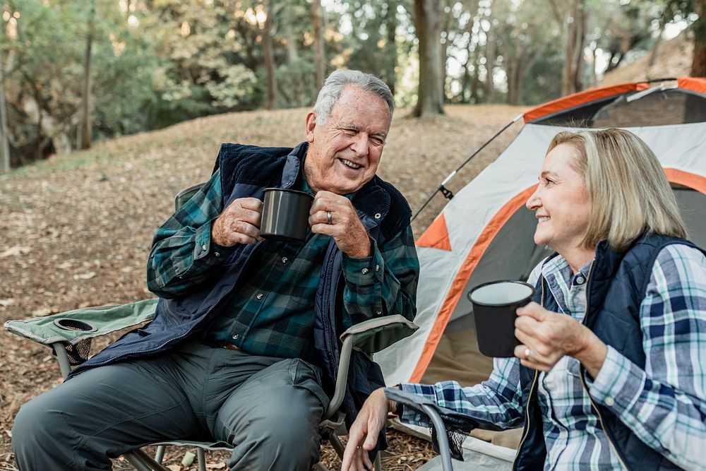 Happy senior couple having coffee by the tent in the forest