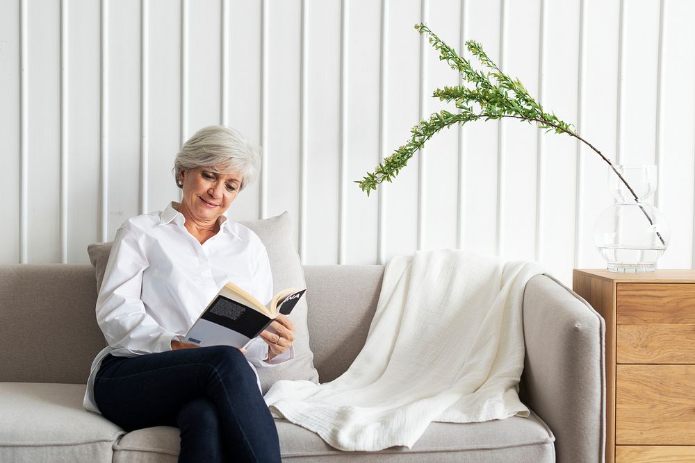 Senior woman reading a book on the sofa in a Scandinavian decor living room