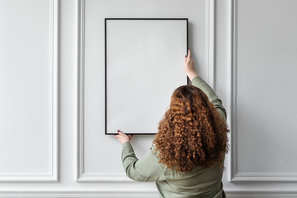 Woman hanging blank picture frame on the wall