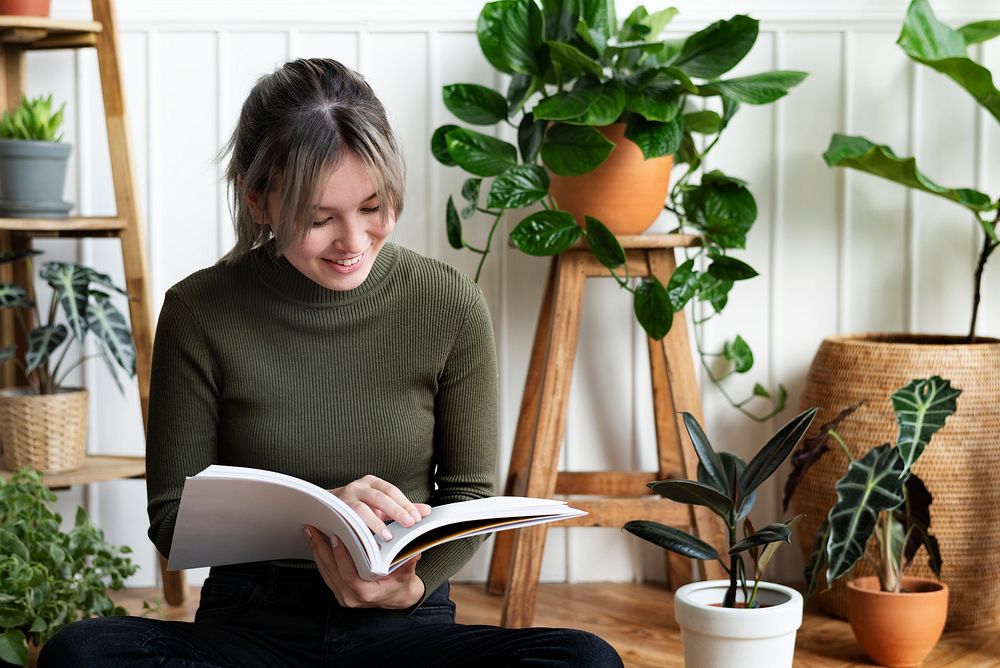 Young woman reading a book about gardening surrounded by potted plants