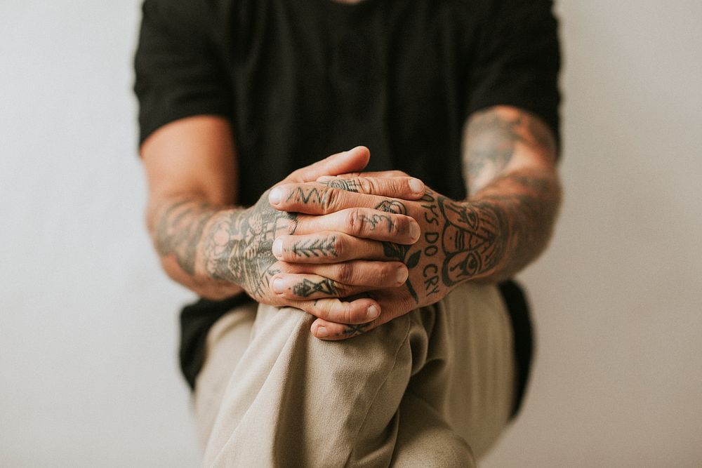 Tattooed man with hands clasping his knees. 2 OCTOBER 2020 - CHIPPENHAM, UK