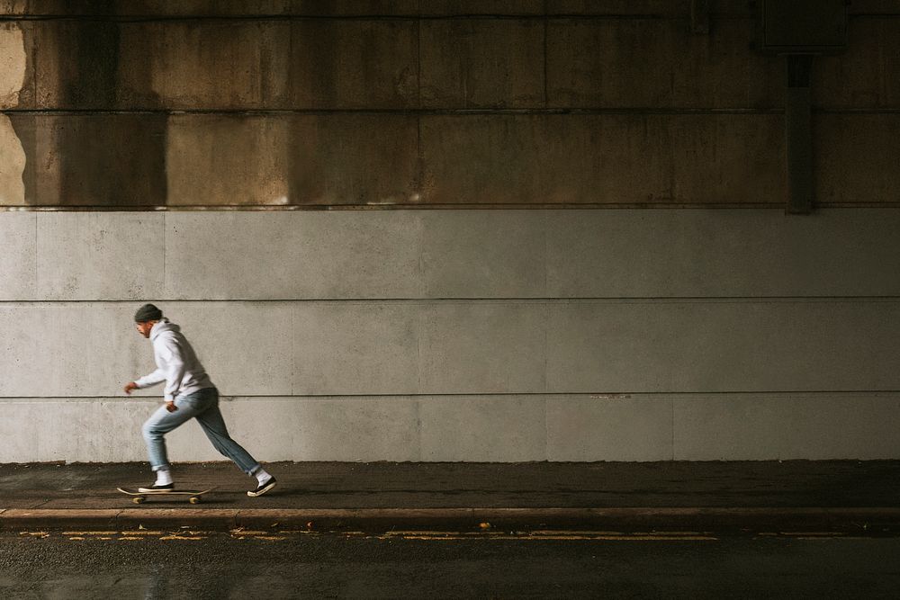 Man skateboarding under a bridge with urban wall design space
