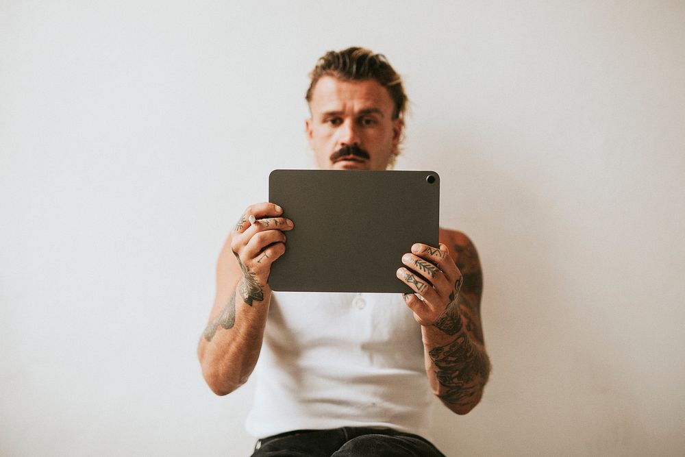 Urban tattooed man in white tank top using digital tablet
