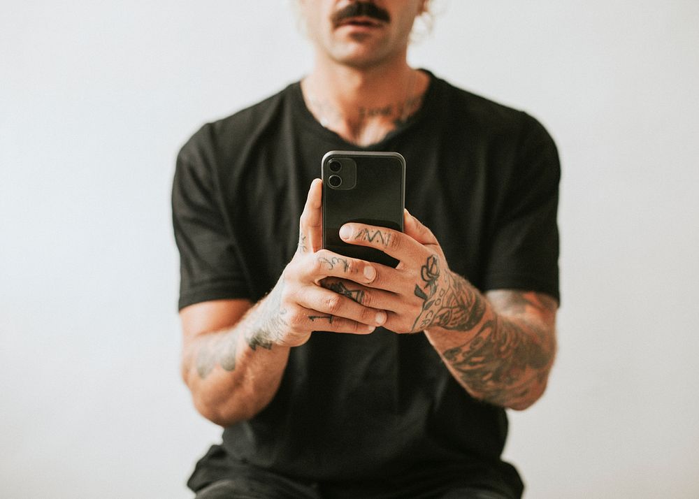 Tattooed man in black tee using smartphone