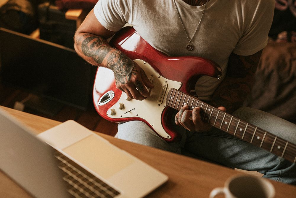 Cool tattooed man playing a guitar in a studio