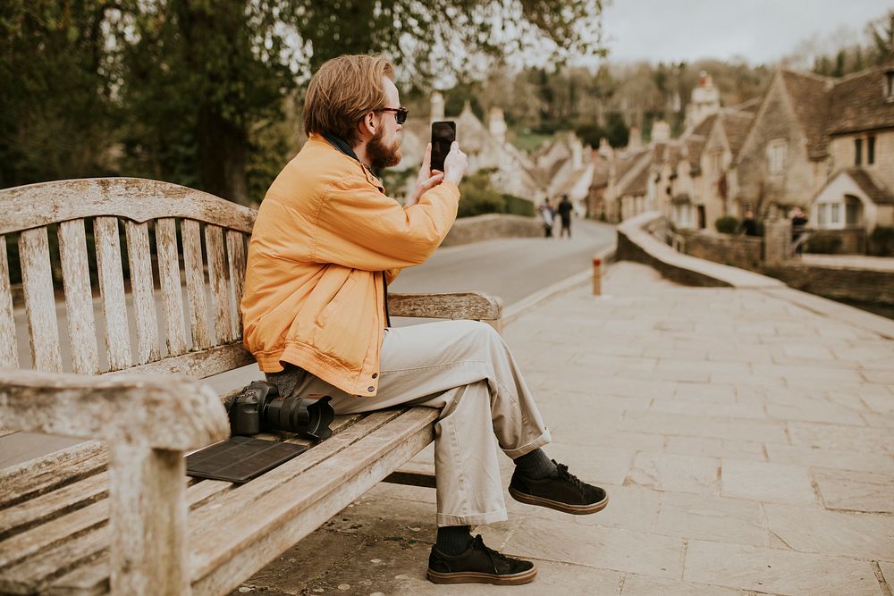 Man sitting on a bench and taking photos on his phone in the village