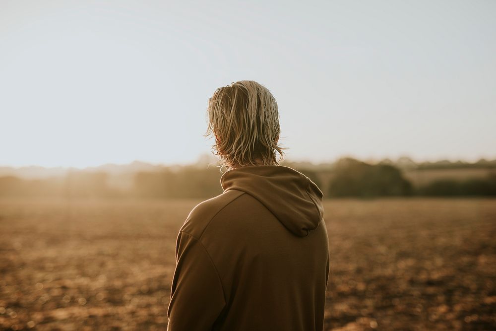 Blonde man in stretchy hoodie watching sunset in the countryside