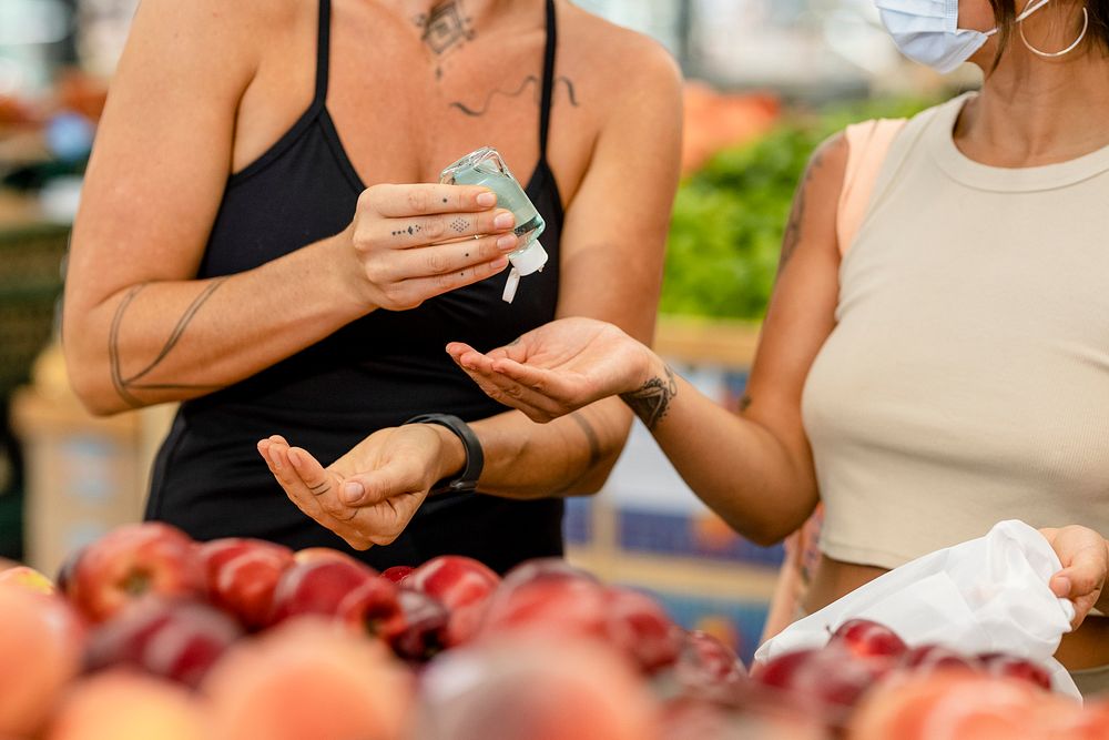 Women sharing hand sanitizer, grocery shopping image