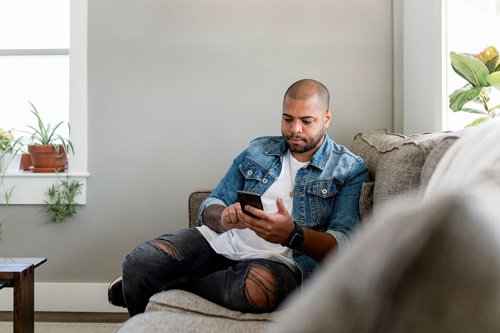Man texting on smartphone, sitting on a couch at home