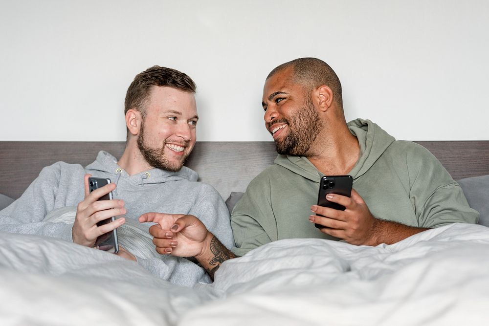 Happy gay couple image, on their phones in bed