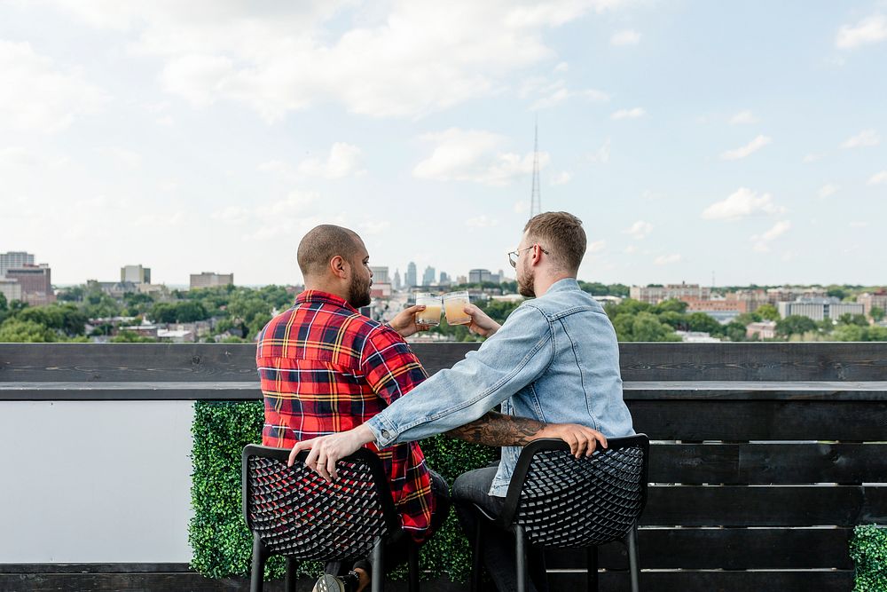 Gay couple cheering glass, on a rooftop bar date