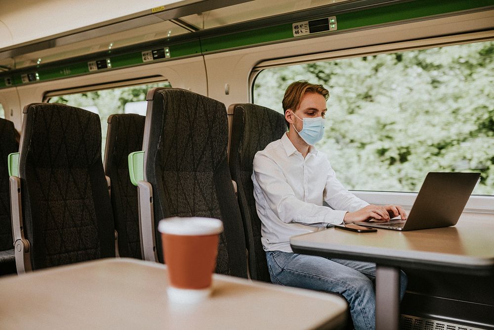 Man wearing mask using laptop on a train in the new normal