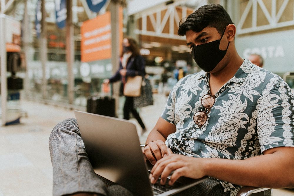 Man wearing mask using a laptop at a train station in the new normal