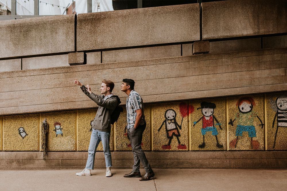 Friends taking selfie by a street art mural graffiti by UK artist Stik at South Bank, Waterloo, London, United Kingdom taken…