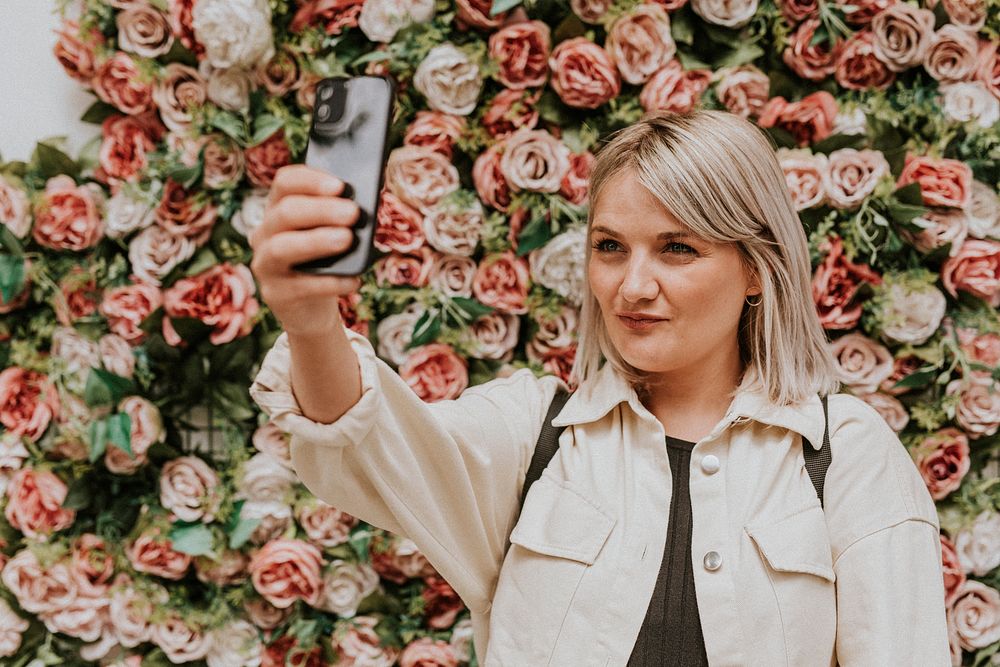 Woman taking a selfie by the flower wall installation