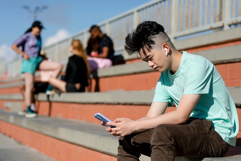 Teen boy using smartphone alone, away from friends
