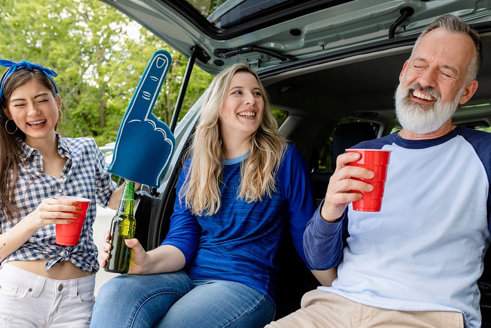 Baseball fans sitting and drinking in the car boot at a tailgate party