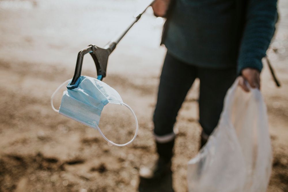 Beach cleanup volunteer picking up face mask for environment campaign
