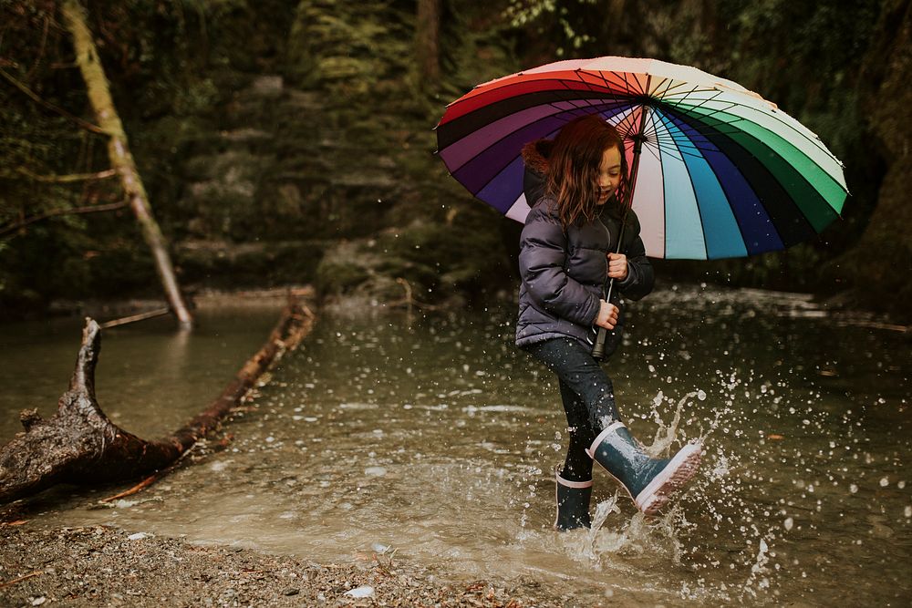 Happy girl playing by the forest lake with an umbrella on a rainy day