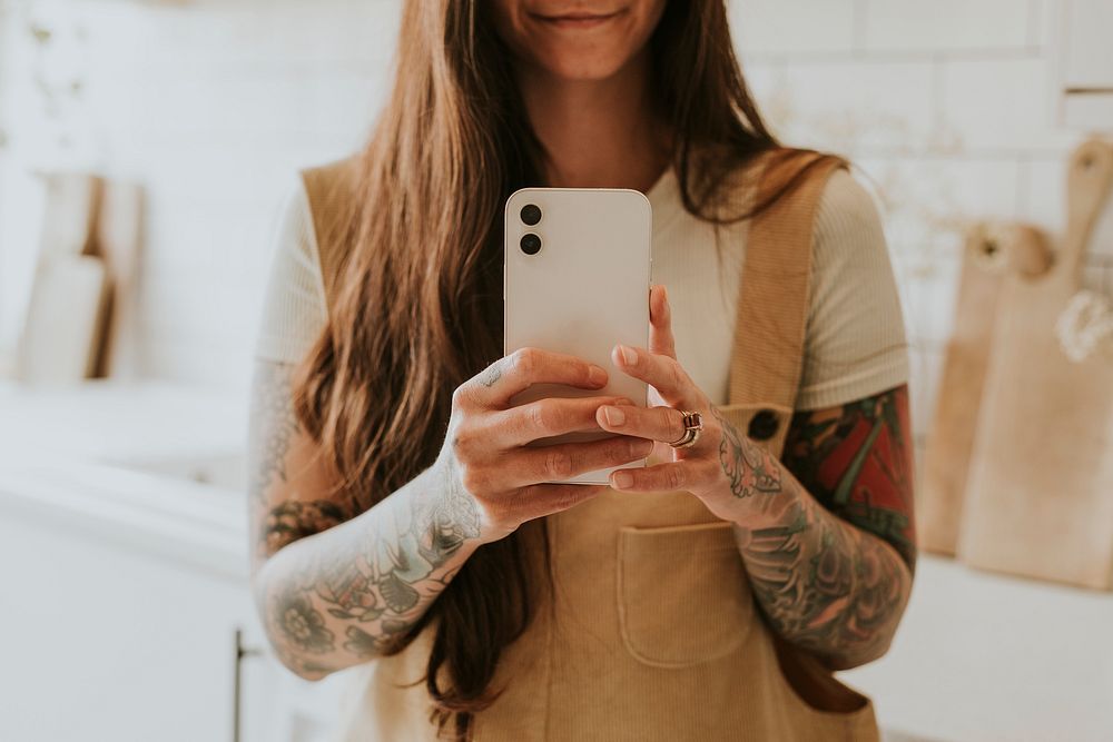 Tattooed woman smartphone in a bright kitchen