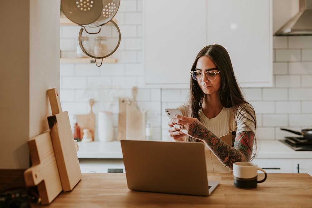 Tattooed woman using her phone and laptop at home