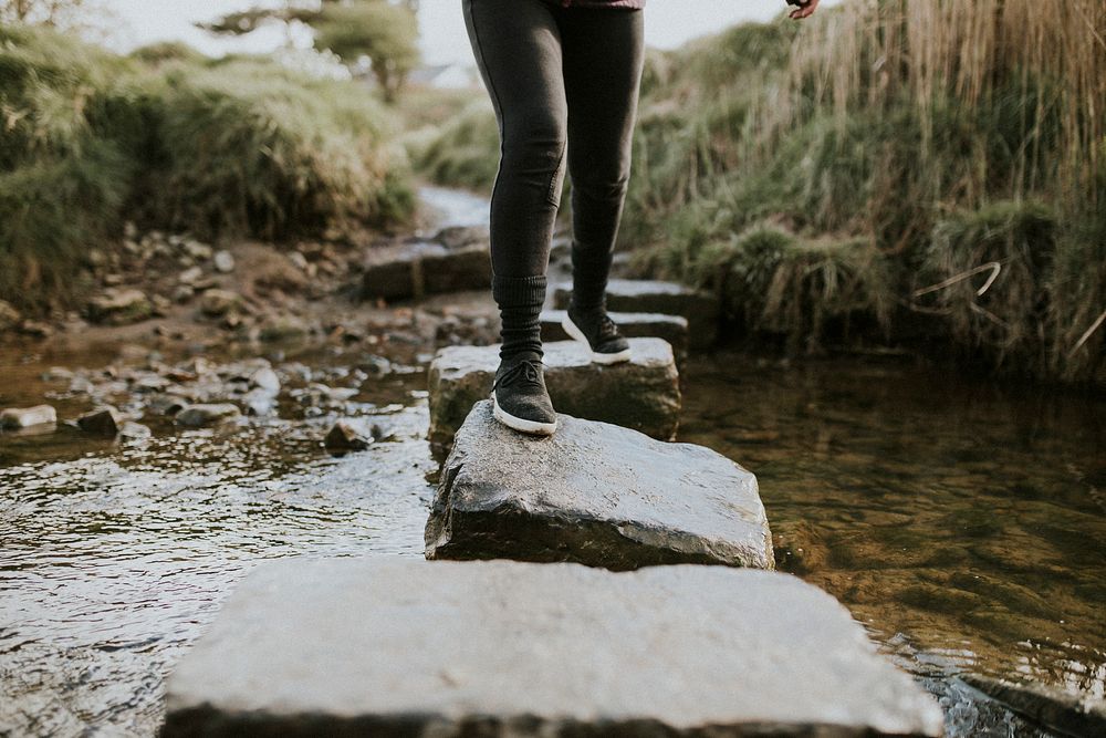 Woman carefully crossing the stream by stepping stone